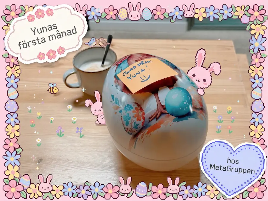 A large decorated Easter egg on a wooden table with a post-it note that says 'GLAD PÅSK YUNA! =)' (Swedish for 'Happy Easter Yuna'). Next to it is a coffee cup. The image is framed by a cute pixel-art frame with flowers and bunnies, along with the text 'Yunas första månad hos MetaGruppen' (Swedish for 'Yuna's first month at MetaGruppen').